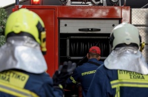 Πυροσβέστες φορούν τη στολή τους και στέκονται πίσω από όχημα, έτοιμοι να επιχειρήσουν για την κατάσβεση φωτιάς