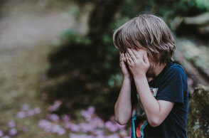 Ένα μικρό αγόρι κρύβει το πρόσωπό του με τα χέρια του