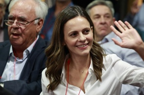 Η Έφη Αχτσιόγλου με σηκωμένο το χέρι χαιρετά και χαμογελά