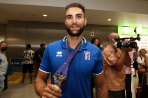 Ο Στέφανος Ντούσκος κρατώντας ένα μεταλλείο φορώντας μπλε αθλητική μπλούζα