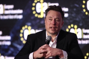 Ο Έλον Μασκ καθιστός με ένα μικρόφωνο στο χέρι σε συνέντευξη