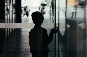 Σκιά ενός μικρού αγοριού που αγγίζει μια τζαμαρία έχοντας γυρισμένη την πλάτη στο φακό