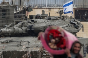 Παλαιστίνιος κουβαλώντας ρούχα μπροστά από τανκ του Ισραήλ