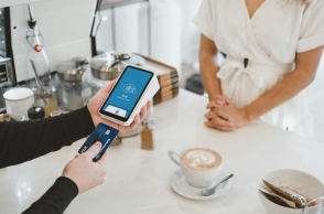 Δύο χέρια σκανάρουν κάρτα σε pos μπροστά από γυναίκα με άσπρο φόρεμα