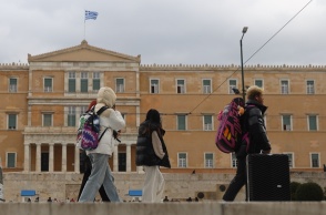 Άτομα με ζεστά ρούχα και μπουφάν περπατούν μπροστά από τη Βουλή