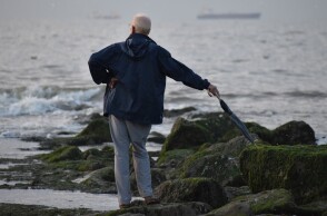 Ηλικιωμένος με ομπρέλα στην ακτή με φόντο τη θάλασσα