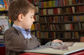 boy sitting near red table reading book