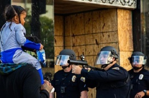 Αστυνομικός σημαδεύει με το όπλο του Αφροαμερικανό που κρατά στους ώμους ένα μικρό κοριτσάκι