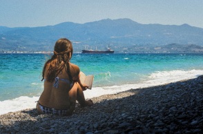 Κοπέλα διαβάζει βιβλίο μπροστά στη θάλασσα