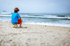 Αγόρι που κάθεται πάνω σε μια μπάλα σε παραλία