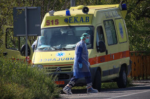 Τραυματιοφορέας με προστατευτική στολή για κορωνοϊό περνά μπροστά από ασθενοφόρο του ΕΚΑΒ