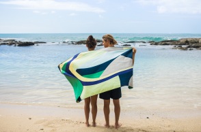 Άντρας και γυναίκα στέκονται με γυρισμένη πλάτη όρθιοι σε παραλία, τυλιγμένοι με μια πετσέτα