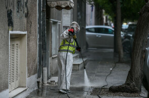 Υπάλληλος του Δήμου Αθηναίων με προστατευτική στολή για τον κορωνοϊό απολυμαίνει πεζοδρόμιο στο κέντρο της Αθήνας