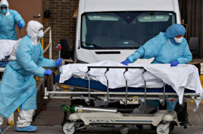 Τραυματιοφορείς στις ΗΠΑ με προστατευτικές στολές για τον κορωνοϊό σπρώχνουν φορείο με τη σορό ασθενούς Covid-19