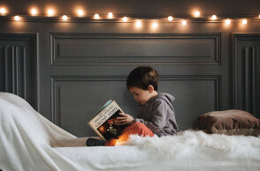 Αγοράκι καθισμένο σε κρεβάτι κρατώνας βιβλίο στα χέρια του