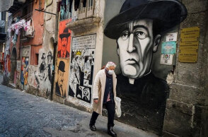 Ιταλία - Covid-19: Άνδρας με προστατευτική μάσκα για τον κορωνοϊό περνά μπροστά από γκράφιτι