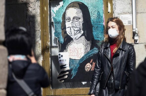 Γυναίκα με προστατευτική μάσκα για τον κορωνοϊό περνά μπροστά από γκράφιτι με την Τζοκόντα