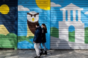 Πολίτες με μάσκα περπατούν μπροστά από κλειστά καταστήματα