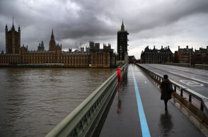 Γυναίκα με μάσκα για τον κορωνοϊό διασχίζει τη γέφυρα Westminster στο Λονδίνο εν μέσω lockdown για τον κορωνοϊό