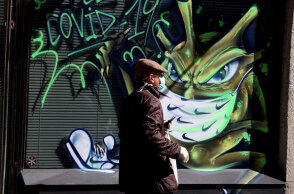 Άνδρας με μάσκα περνά μπροστά από γκράφιτι για τον κορωνοϊό
