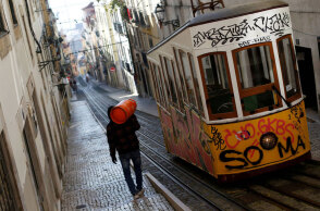Πορτογαλία - Κορωνοϊός: Άνδρας κουβαλά φιάλη υγραερίου στην πλάτη δίπλα από συρμό του τραμ στη Λισαβόνα