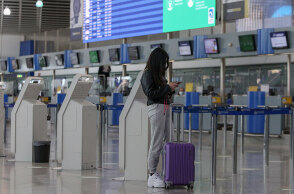 Αεροδρόμιο «Ελευθέριος Βενιζέλος»: Κοπέλα κοιτά το κινητό της μπροστά στον φωτεινό πίνακα για τις πτήσεις εσωτερικού - εξωτερικού