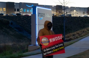 Εργαζόμενος κρατά πλακάτ έξω από αποθήκη της Amazon