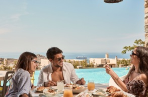 Ένας άντρας και δύο γυναίκες τρώνε πρωινό με φόντο το Αιγαίο