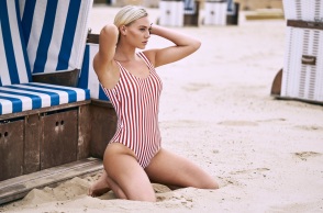 Γυναίκα γονατισμένη στην άμμο με ριγέ ολόσωμο μαγιό