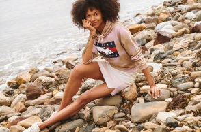 Γυναίκα με φούστ ακαι φούτερ καθισμένη σε βότσαλα δίπλα σε θάλασσα