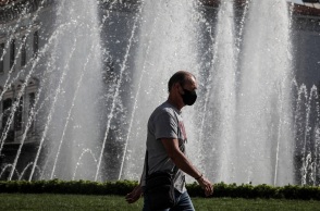 Πολίτης φορά μάσκα προστασίας κατά του κορωνοϊού και περπατά μπροστά από σιντριβάνι