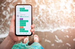 Ανθρώπινο χέρι που κρατά smartphone σε παραλία