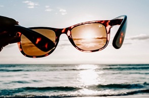 Ένα άτομο κρατάει ένα ζευγάρι γυαλιά ηλίου μπροστά από τη θάλασσα. 