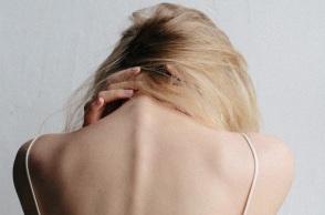 Γυναίκα με γυρισμένη πλάτη και σκυμμένο κεφάλι, κρατάει τον αυχένα της