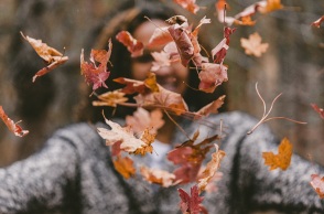 Ένα κορίτσι πετάει στον αέρα φθινοπωρινά φύλλα.