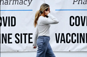 Κοπέλα στις ΗΠΑ μιλά στο κινητό, περνώντας μπροστά από αφίσες για τον εμβολιασμό κατά του κορωνοϊού