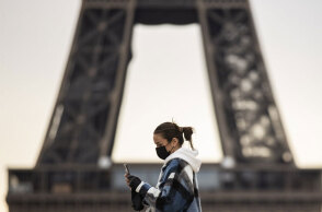 Κοπέλα με μάσκα για τον κορωνοϊό περνά μπροστά από τον Πύργο του Άιφελ στο Παρίσι