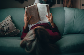 Μια κοπέλα κάθεται ανάποδα στον καναπέ και διαβάζει βιβλίο