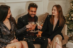 Τρεις φίλοι τσουγκρίζουν τα ποτά τους δίπλα από το χριστουγεννιάτικο δέντρο. 