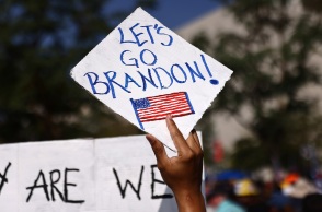 Χέρι που κρατά πινακίδα στην οποία αναγράφεται η φράση Let's Go Brandon