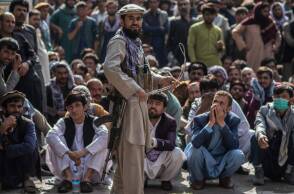 Ένας φρουρός ασφαλείας των Ταλιμπάν κρατάει μαστίγιο ενώ στέκεται μπροστά σε Αφγανούς άνδρες που περιμένουν έξω από μια τράπεζα για να βγάλουν χρήματα 