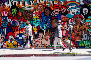 Πολίτες με μάσκα για κορωνοϊό στο Λος Άντζελες μπροστά από mural για το Χόλιγουντ