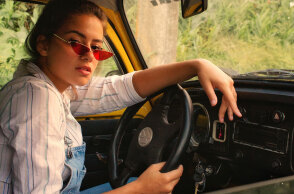 Γυναίκα καθισμένη σε αυτοκίνητο, κρατάει τιμόνι και κοιτάζει την κάμερα