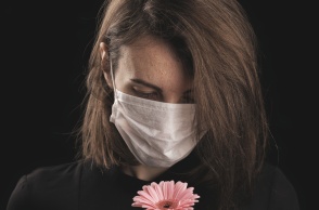 Γυναικά με μάσκα κρατά στα χέρια της ένα λουλούδι