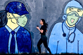 Κοπέλα κάνει τζόκινγκ, περνώντας μπροστά από mural για τον κορωνοϊό