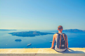 Άνδρας με σακίδιο πλάτης καθισμένος σε πεζούλι με φόντο τη θάλασσα