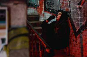 Άντρας με μαύρο φούτερ, κάθεται στα σκαλιά και καπνίζει