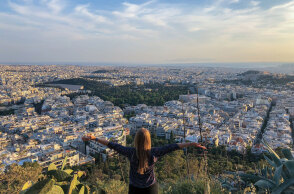 Κοπέλα στέκεται όρθια με γυρισμένη πλάτη με φόντο την Αθήνα από ψηλά