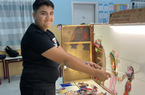 Ο Χρυσοβαλάντης Καραγιαννόπουλος με τις φιγούρες Καραγκιόζη πίσω από τον μπερντέ