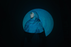 Γυναίκα που φοράει χιτζάμπ, στέκεται μπροστά από μαύρο τοίχο